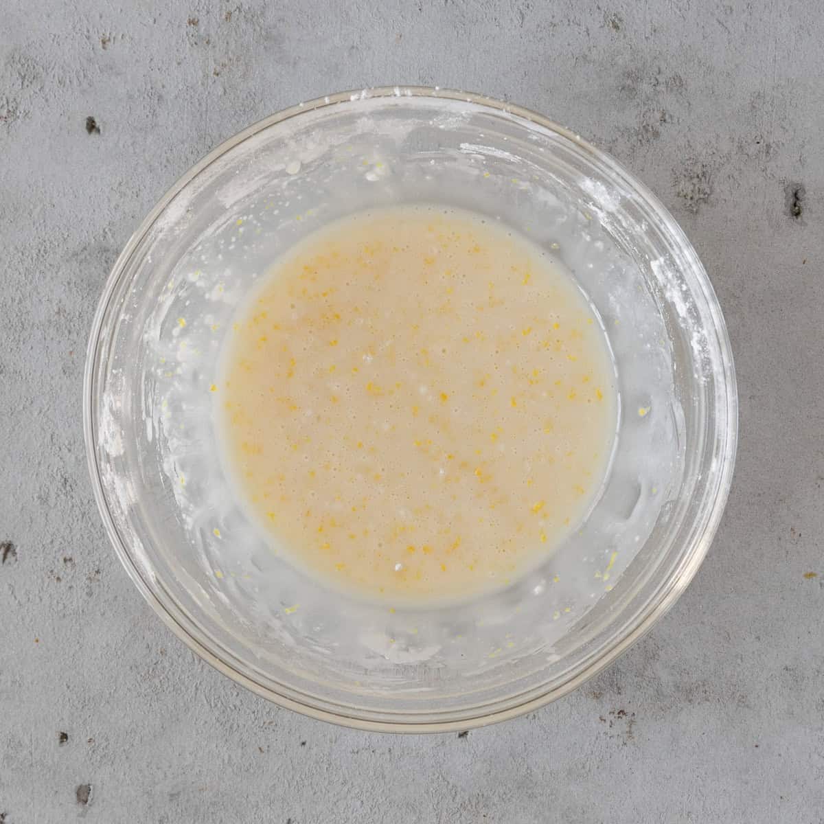 the lemon glaze in a glass bowl on a grey background.