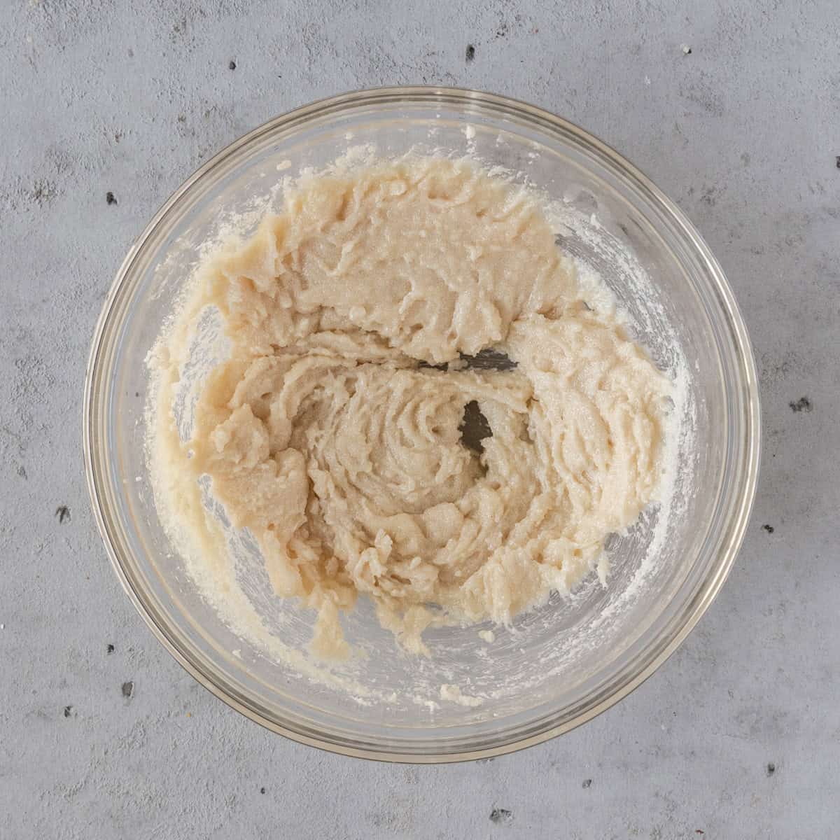 the sugar and butter combined in a glass bowl on a grey background.