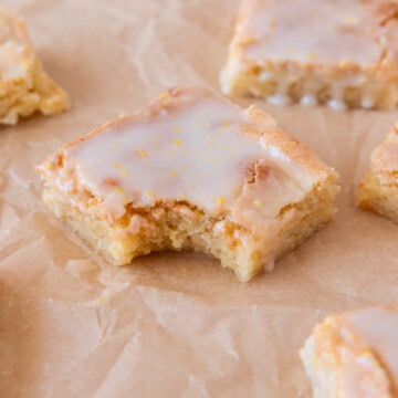 several lemon brownies on a piece of parchment paper. One has a bite out of it.