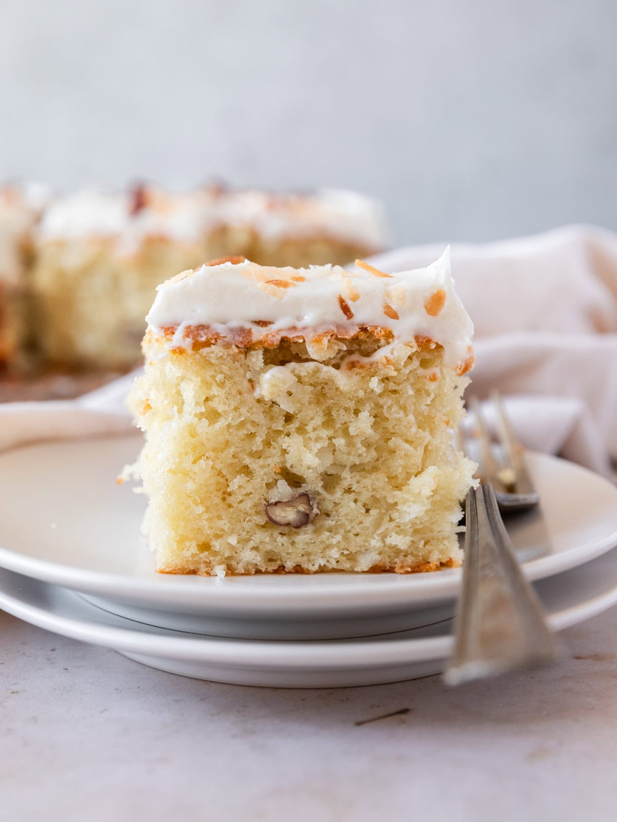 a slice of italian cream cake on a white plate with a fork beside it.