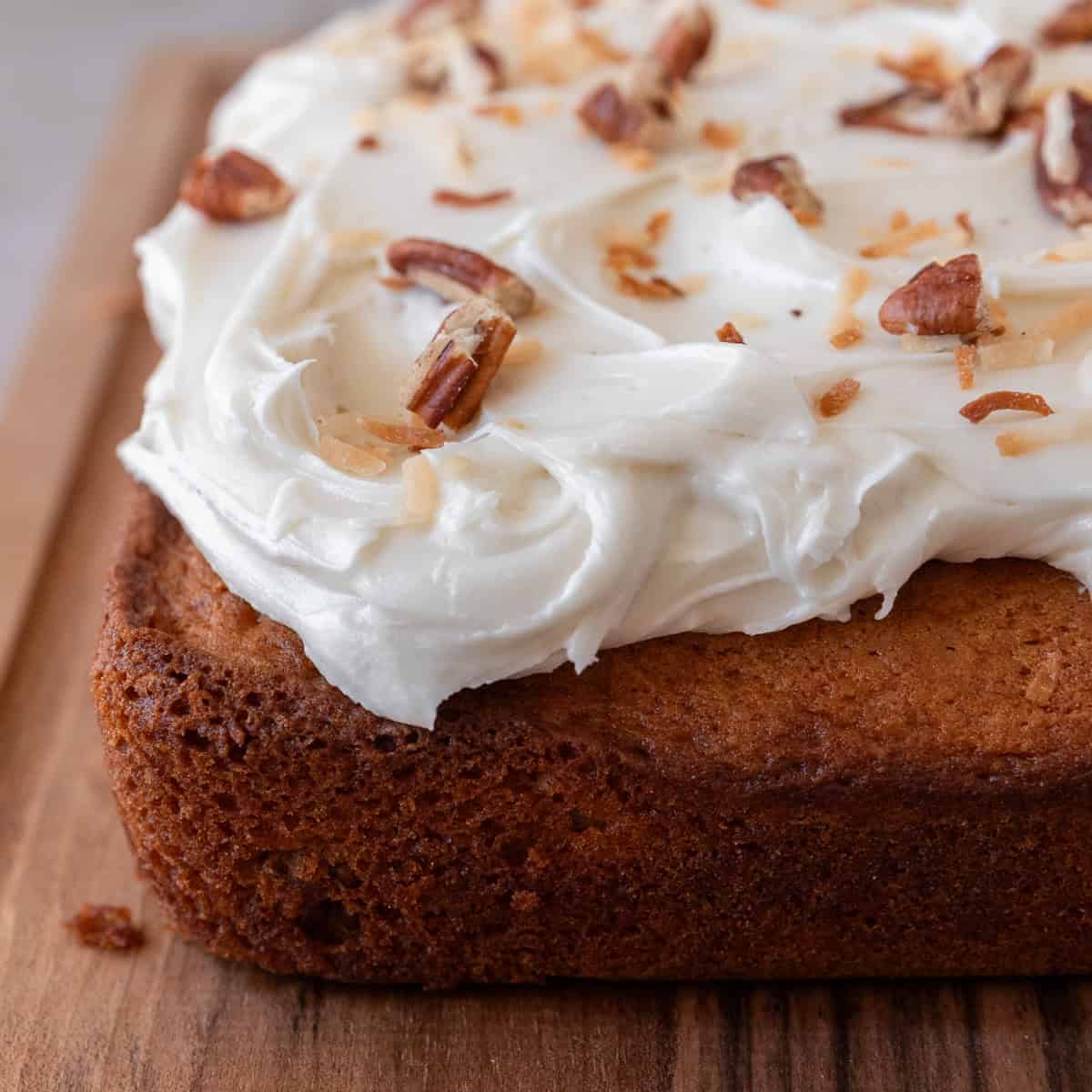 an italian cream cake on a wooden board sprinkled with pecans and shredded coconut.