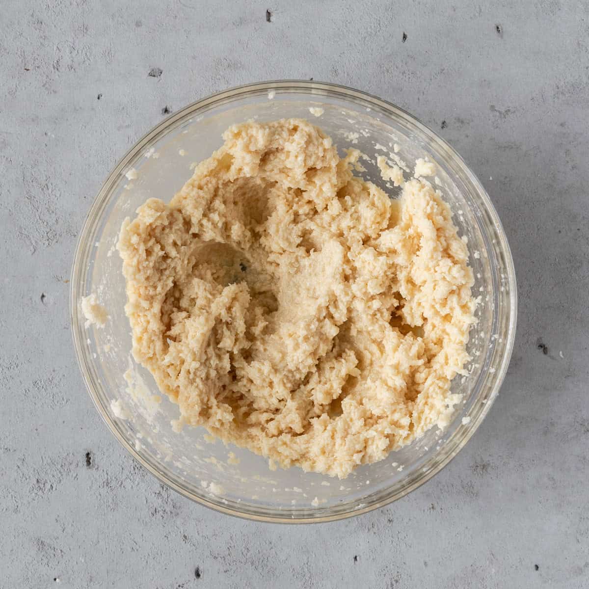 the sugar and wet ingredients combined in a glass bowl on a grey background.