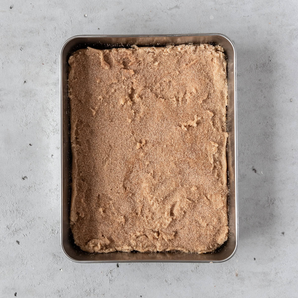 the cookie dough sprinkled with the cinnamon sugar mixture in a baking pan before being baked.