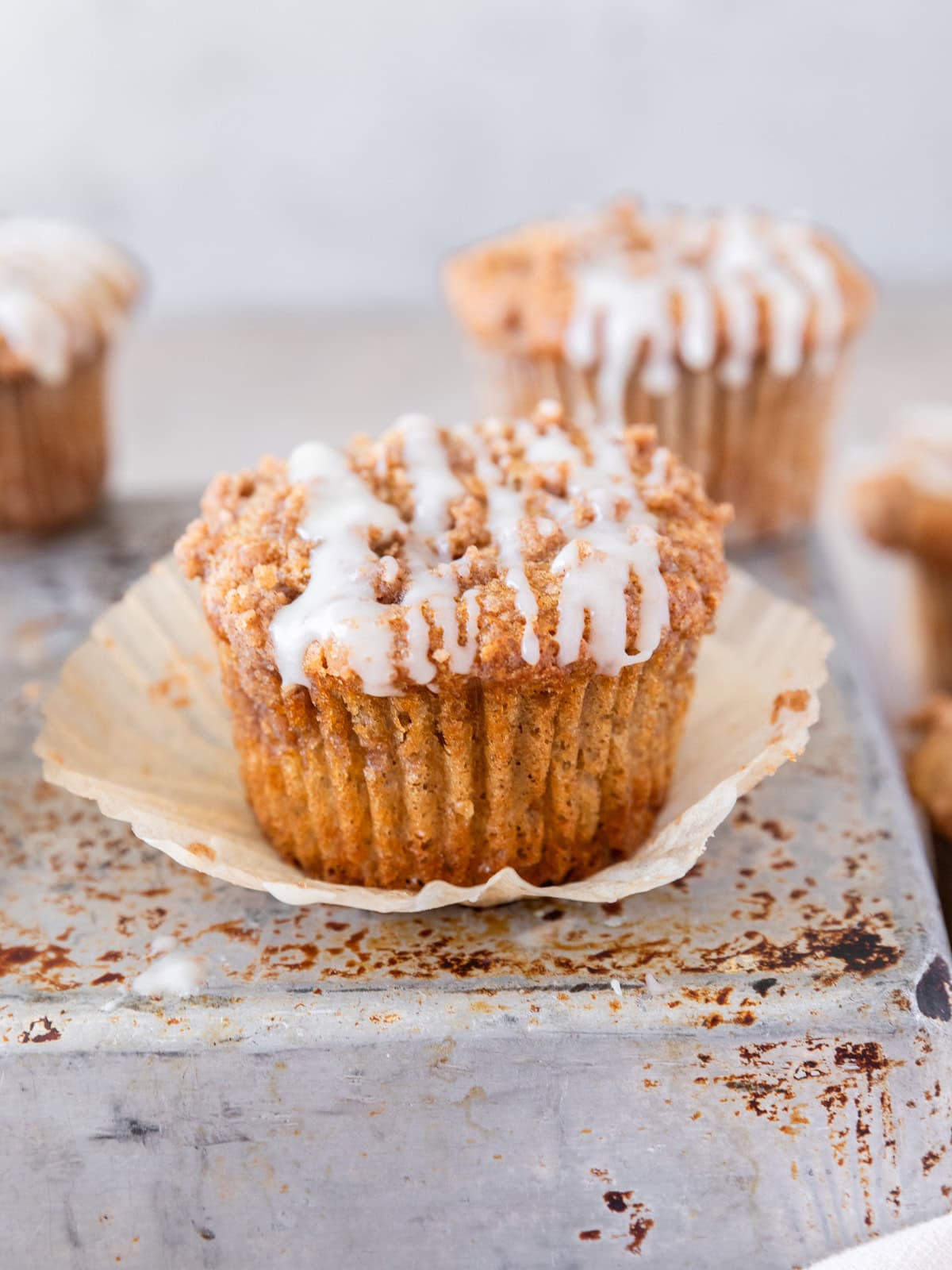 several coffee cake muffins on a metal tin. One has the muffin wrapper pulled off of it.