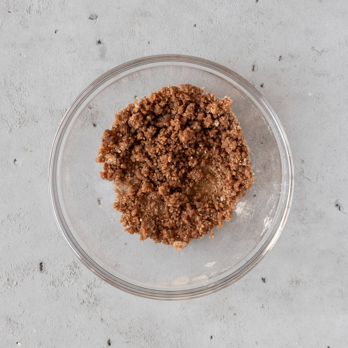 the cinnamon crumble topping in a glass bowl on a grey background.