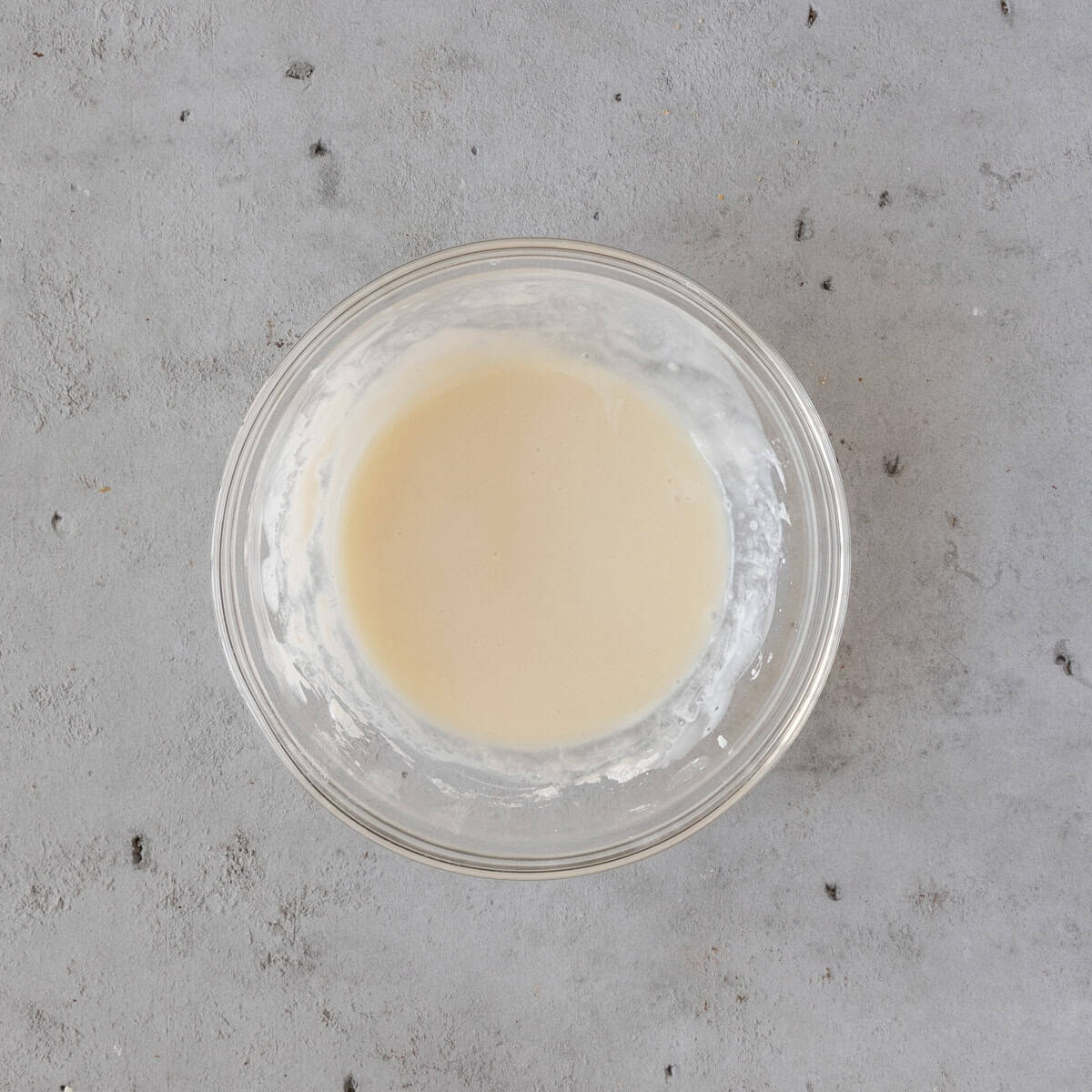 the vanilla icing in a glass bowl on a grey background.