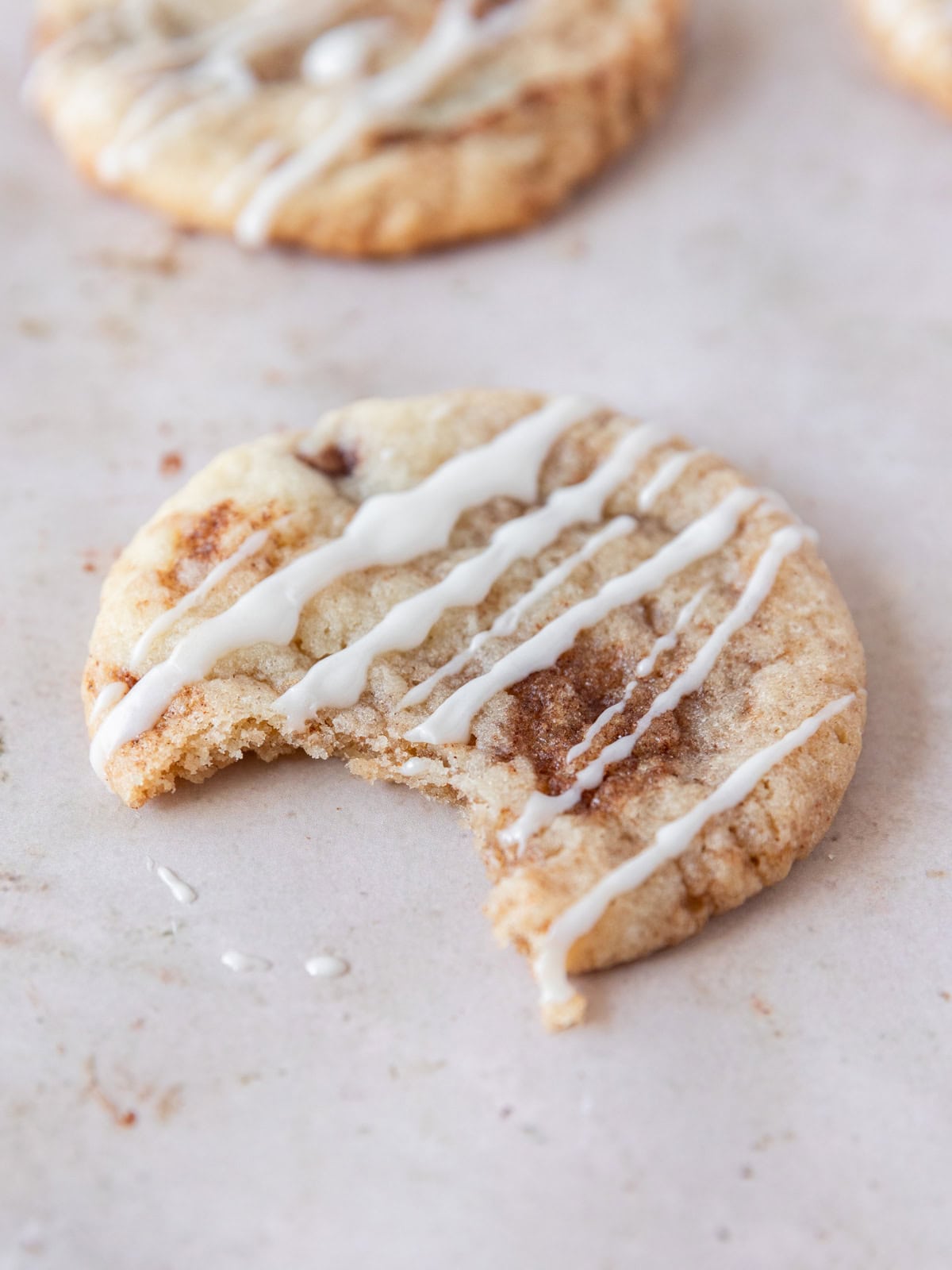 a cinnamon roll cookie with a bite out of it on a tan background.