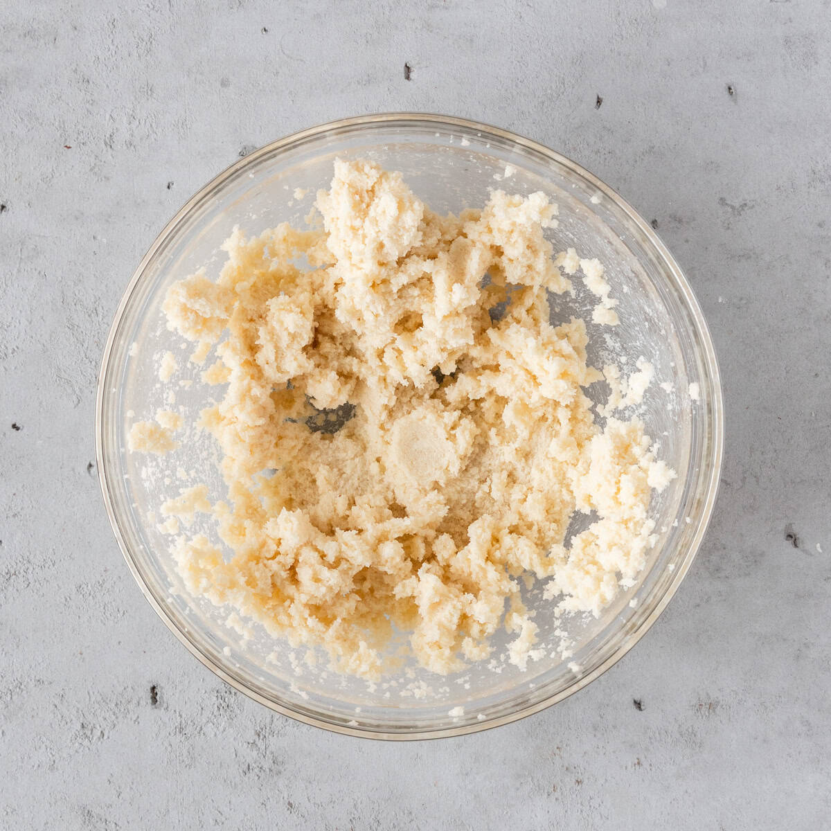 the butter and sugar combined in a glass bowl on a grey background.