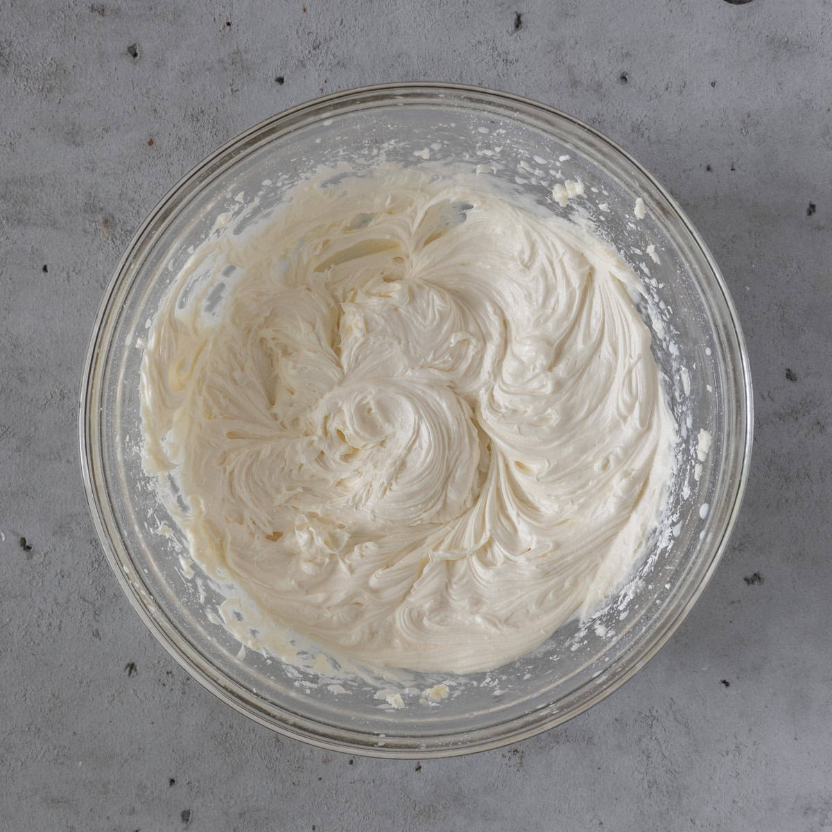 the vanilla buttercream frosting in a glass bowl on a grey background.