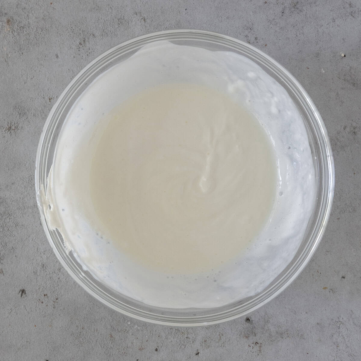 the buttercream and sour cream combined in a glass bowl on a grey background.