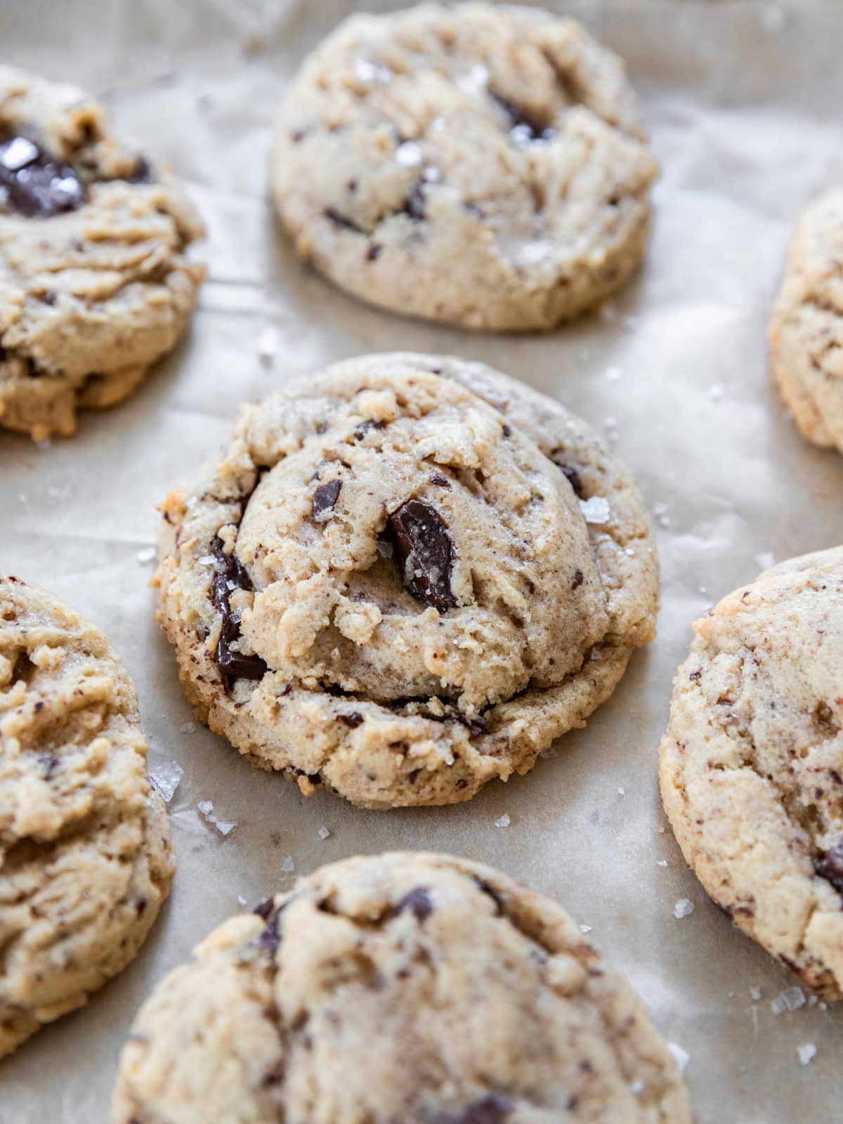 several gooey chocolate chip cookies on a piece of parchment paper.