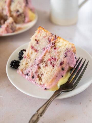 a slice of lemon blackberry cake on a white plate with a metal fork beside it.