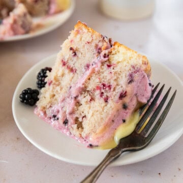 a slice of lemon blackberry cake on white plate with a metal fork beside it.