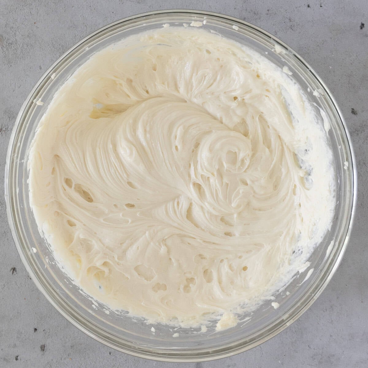 the cream cheese and sugar combined in a glass bowl on a grey background.