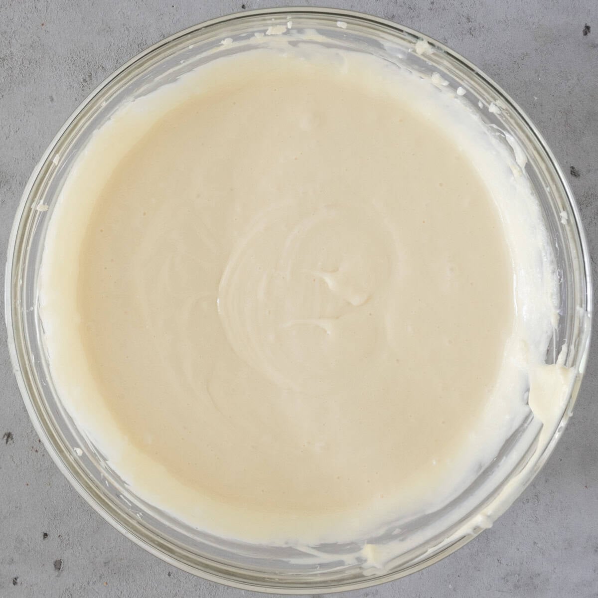 the eggs added to the cheesecake batter in a glass bowl on a grey background.