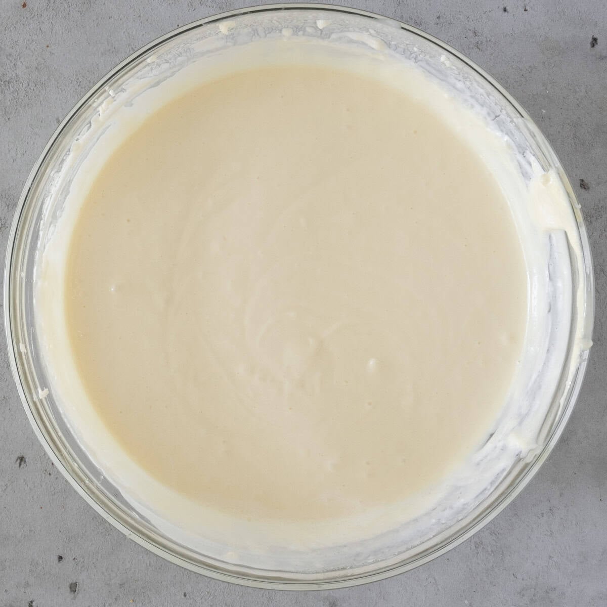 the heavy cream added to the cheesecake batter in a glass bowl on a grey background.