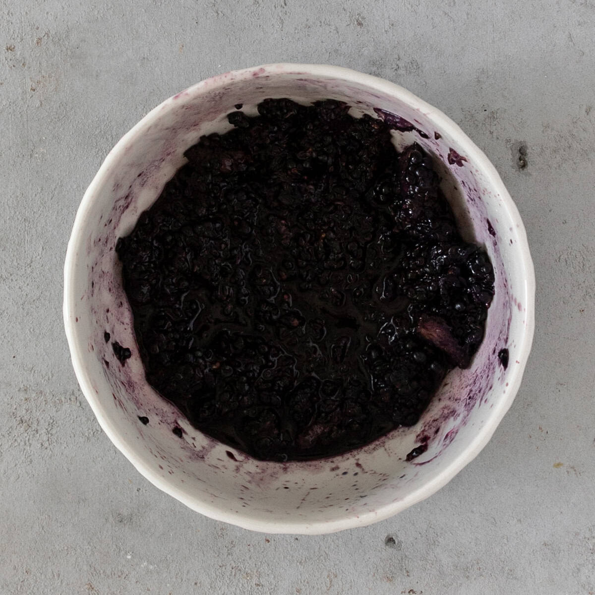 the roughly mashed blackberries in a white bowl on a grey background.