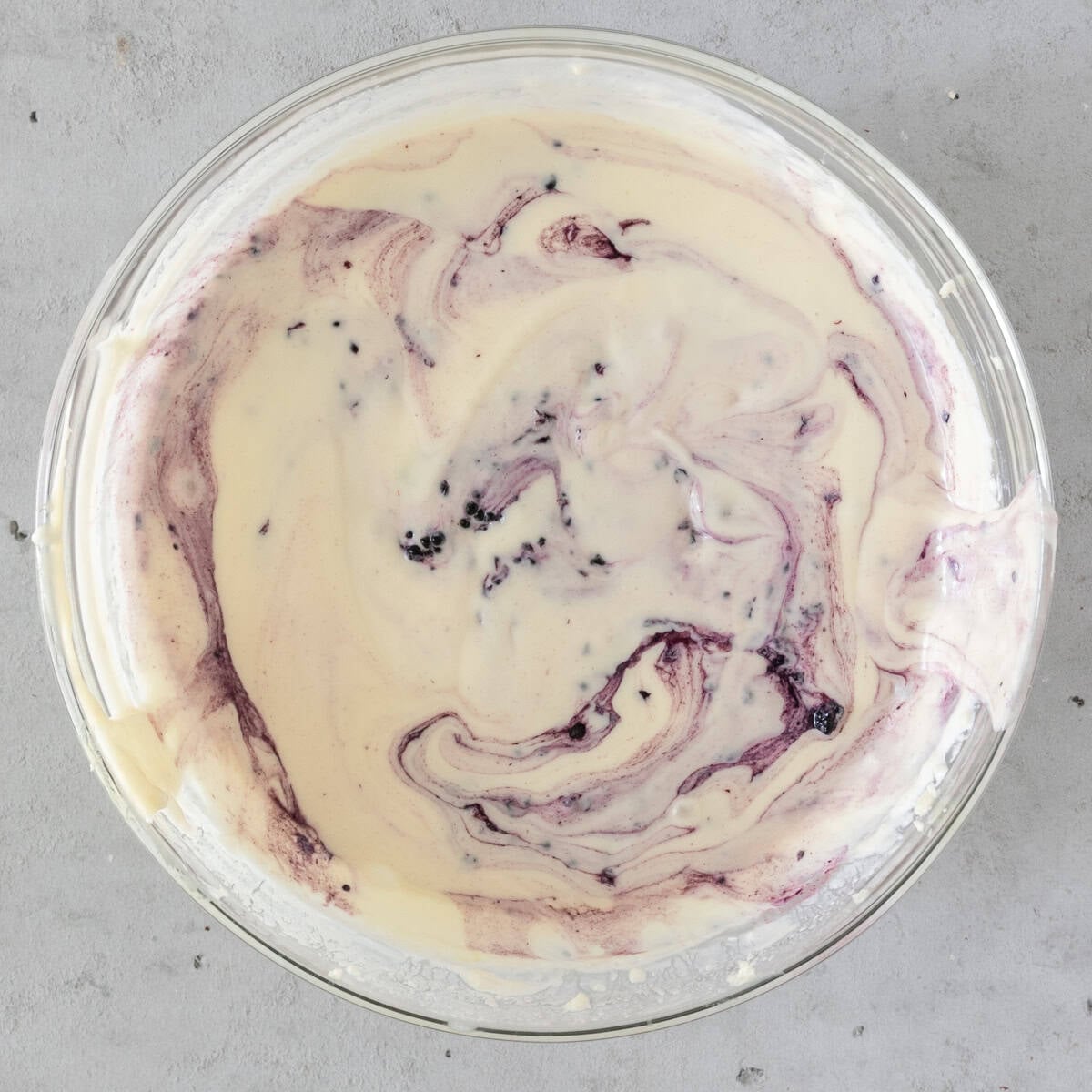 the completed lemon blackberry cheesecake batter in a glass bowl on a grey background.