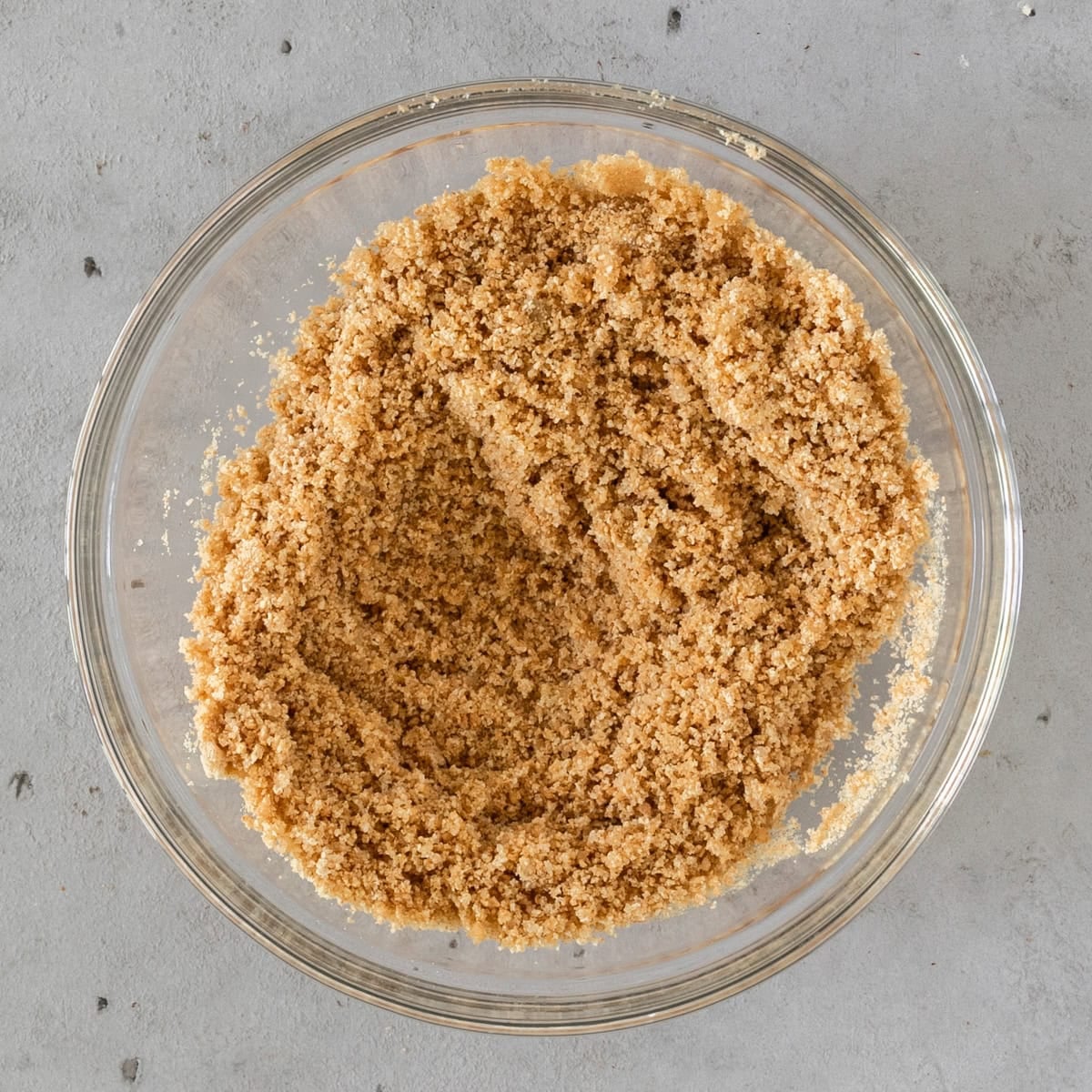 the graham cracker crust ingredients combined in a glass bowl on a grey background.