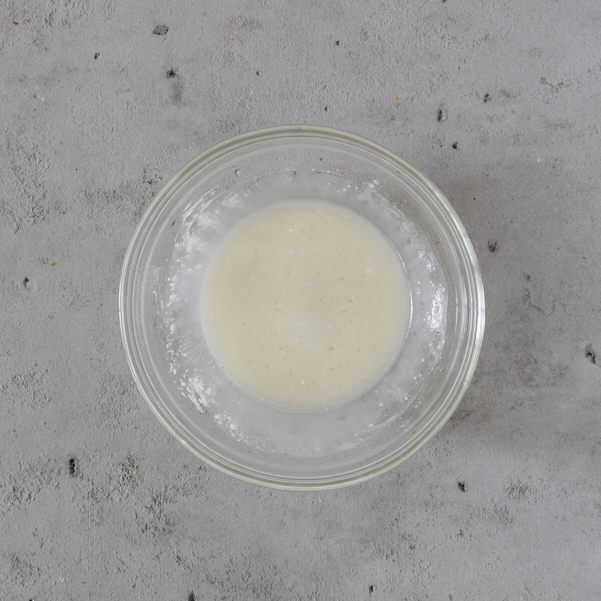 the lemon glaze in a glass bowl on a grey background.