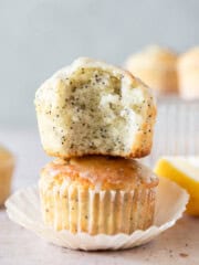 two moist lemon poppy seed muffins stacked on top of each other. One has a bite out of it.