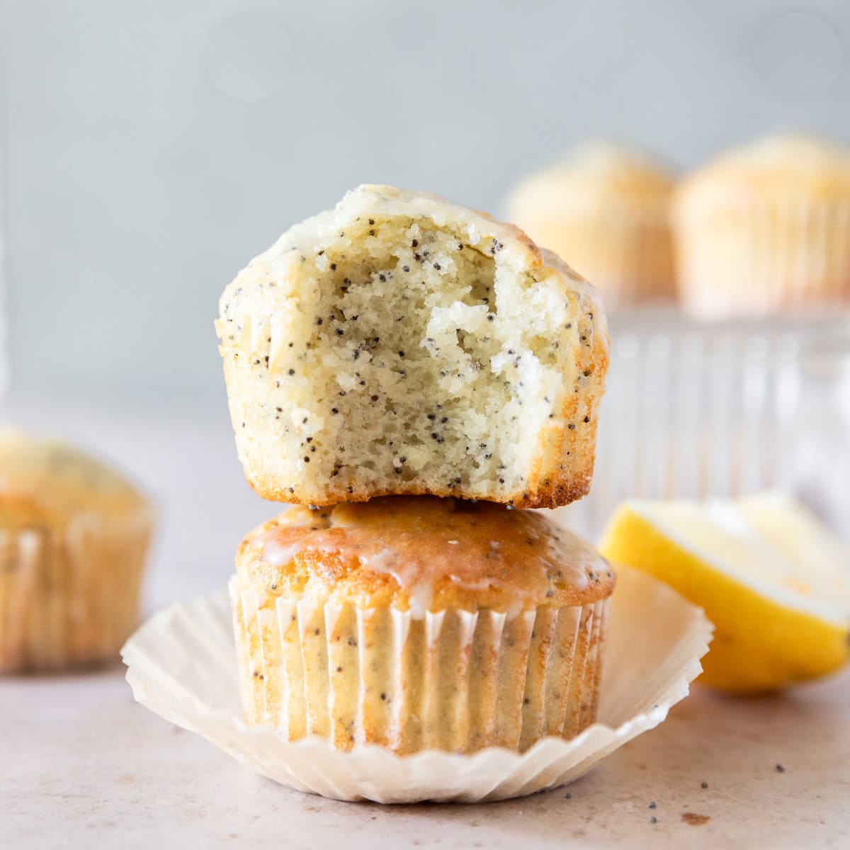 two moist lemon poppy seed muffins stacked on top of each other. One has a bite out of it.