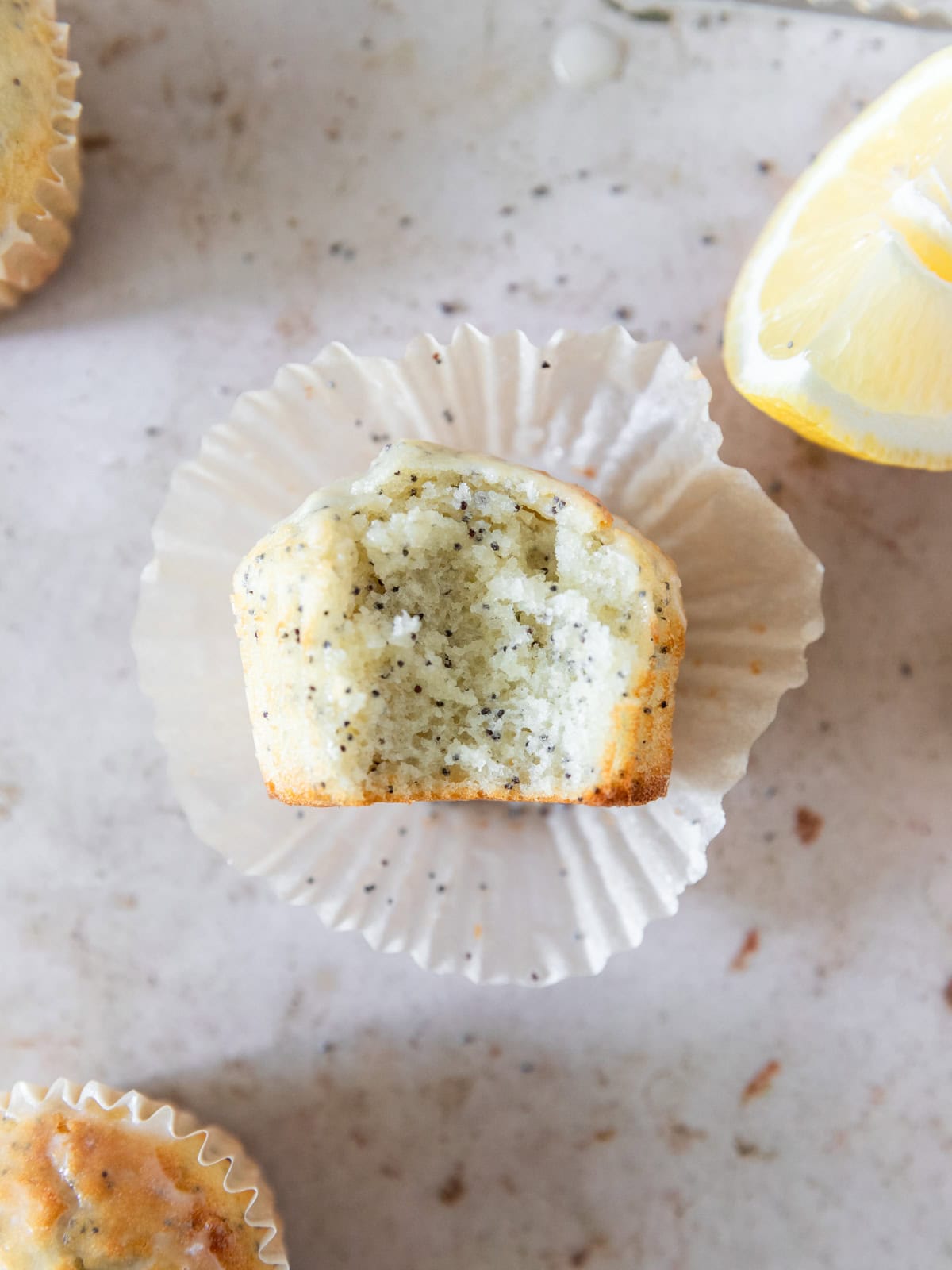a moist lemon poppy seed muffin with lemon glaze laying on top of a muffin liner with a bite out of it.