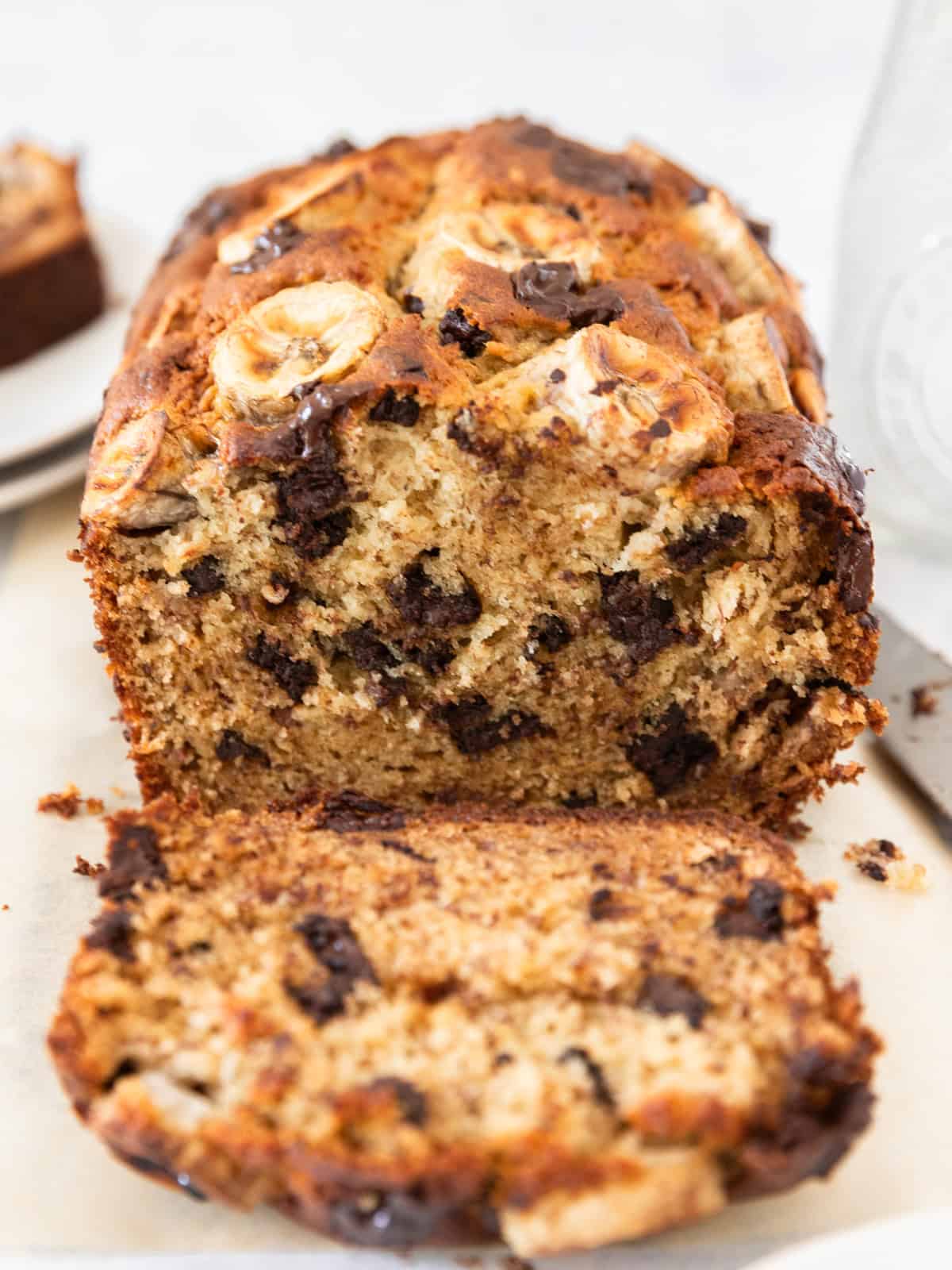 a loaf of moist chocolate chunk banana bread with a slice cut off and laying in front of it.