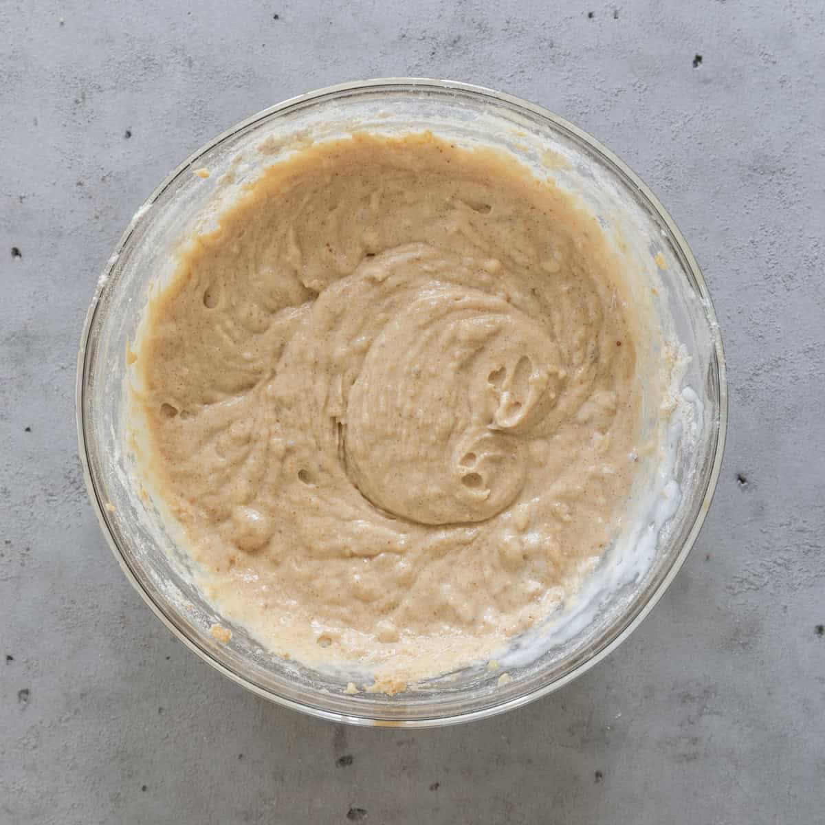 the banana bread batter after the buttermilk and sour cream have been added in a glass bowl on a grey background.