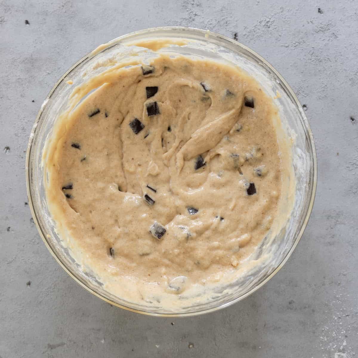 the completed chocolate chunk banana bread batter in a glass bowl on a grey background.