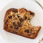 a slice of moist banana bread with chocolate chunks with a bite out of it laying on a white plate.