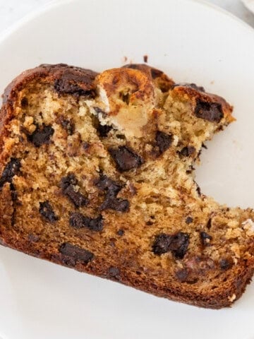 a slice of moist banana bread with chocolate chunks with a bite out of it laying on a white plate.