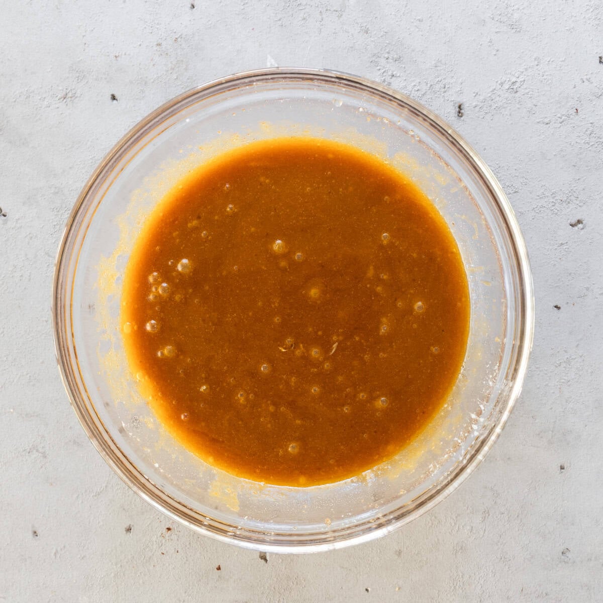 the wet ingredients and sugars combined in a glass bowl on a grey background.