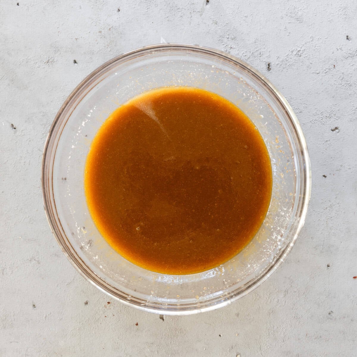 the melted butter and sugar combined in a glass bowl on a grey background.