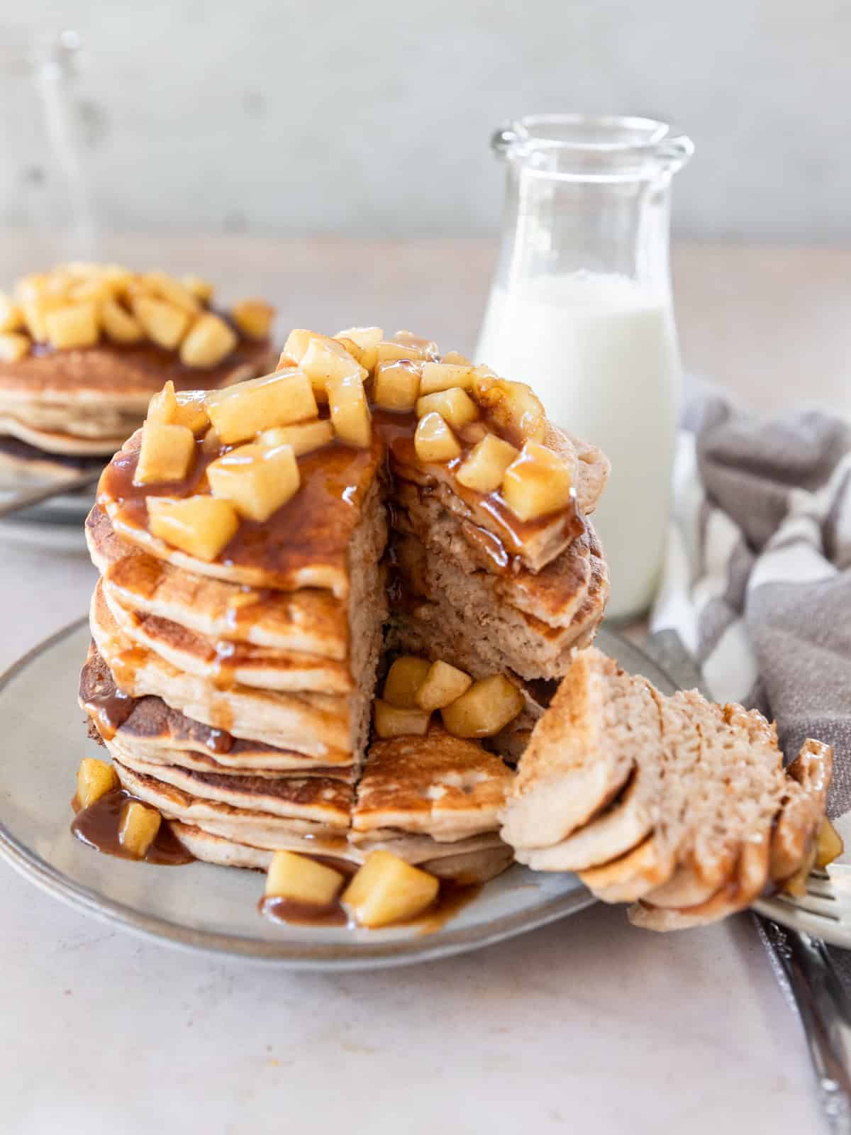 a stack of fluffy apple cinnamon pancakes with a large slice taken out of it.