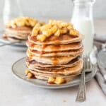 a large stack of fluffy apple cinnamon pancakes on a grey plate with a metal fork beside it.