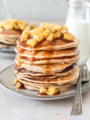 a large stack of fluffy apple cinnamon pancakes on a grey plate with a metal fork beside it.