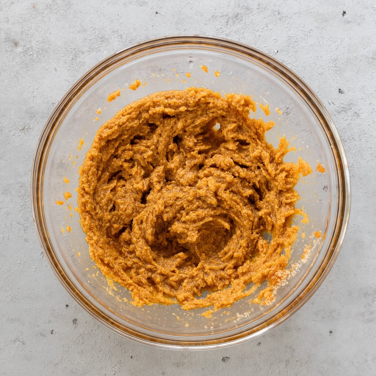 the butter, pumpkin puree, and sugars combined in a glass bowl on a grey background.