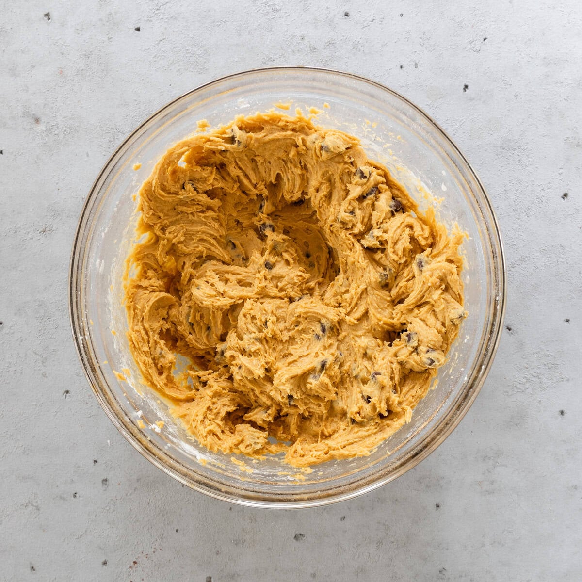 the completed pumpkin chocolate chip cookie dough in a glass bowl on a grey background.