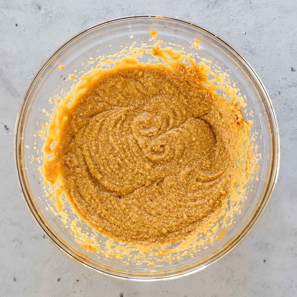 the wet ingredients and sugar combined in a glass bowl on a grey background.