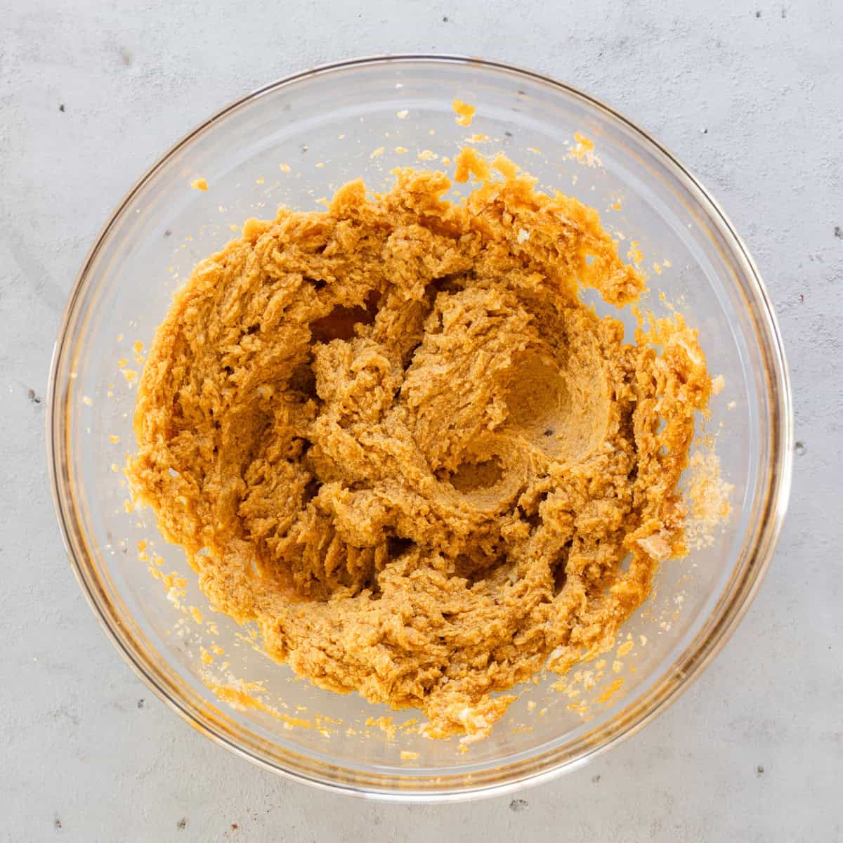 the butter, pumpkin, and sugar combined in a glass bowl on a grey background.