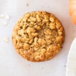 a pumpkin oatmeal cookie with oats and a small pumpkin close to it.