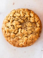a pumpkin oatmeal cookie with oats and a small pumpkin close to it.