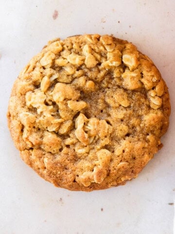 a pumpkin oatmeal cookie with oats and a small pumpkin close to it.