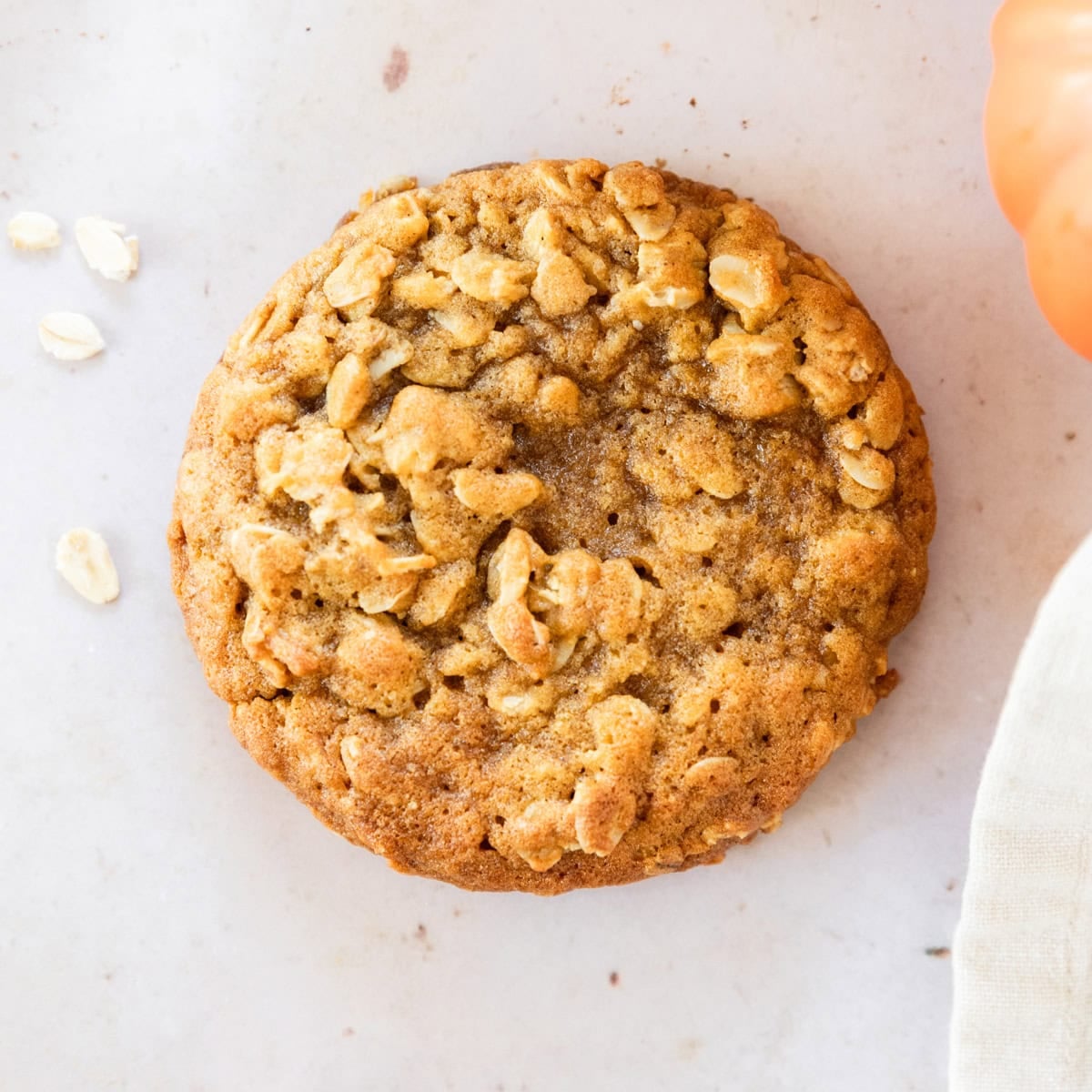 a pumpkin oatmeal cookie with oats and a small pumpkin close to it.