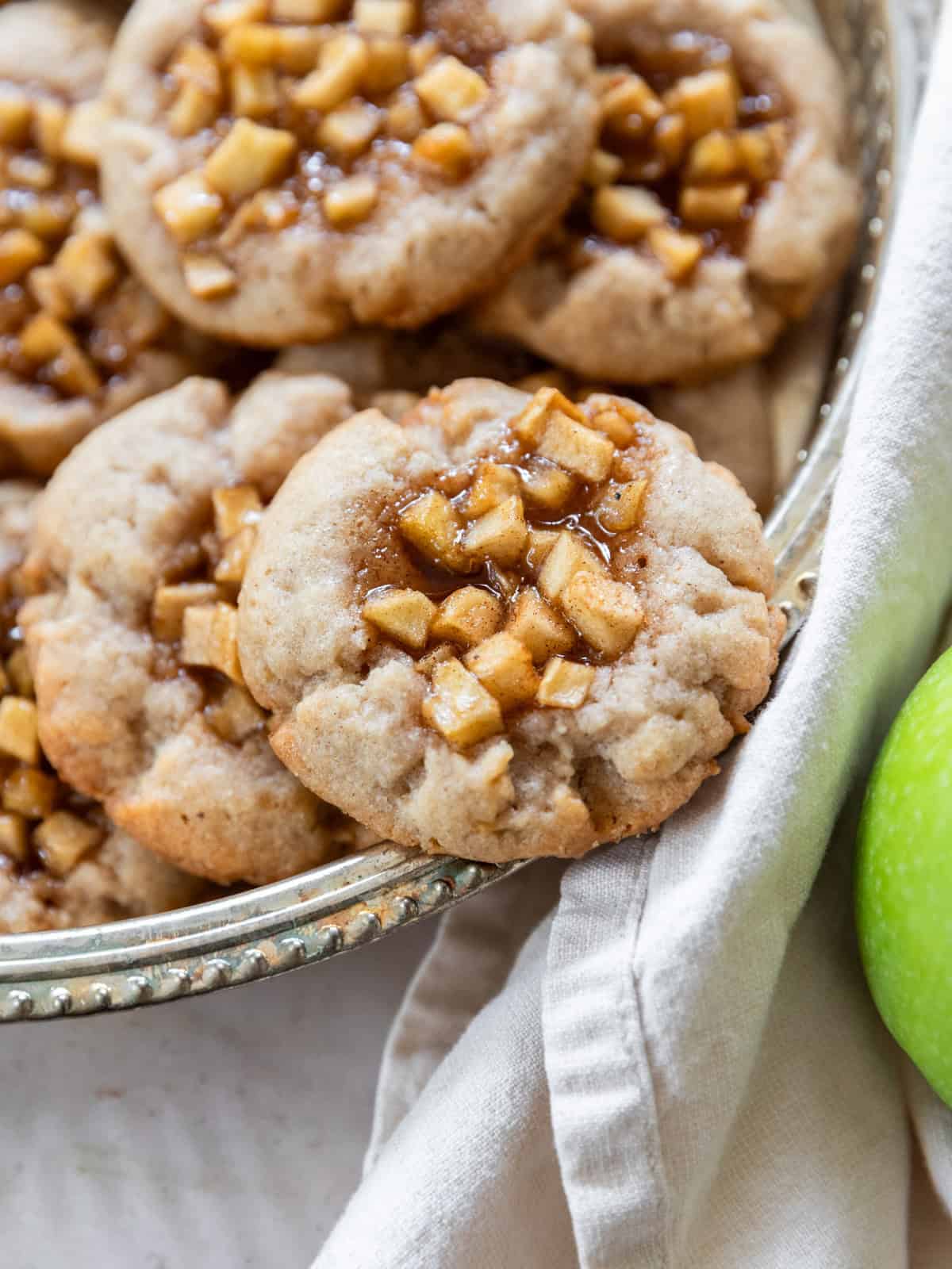 several apple pie cookies on a silver dish with one balancing on the edge.