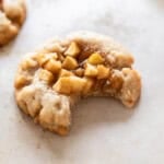 an apple pie cookie with a bite out of it on a tan background.