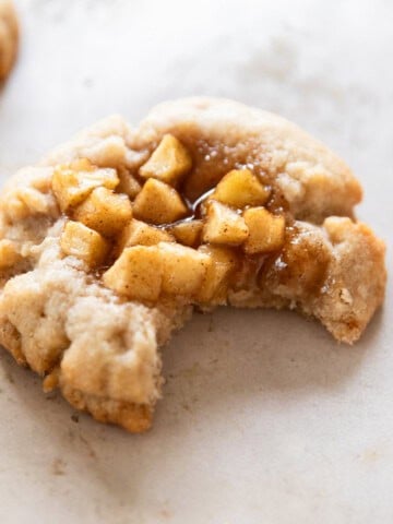 an apple pie cookie with a bite out of it on a tan background.
