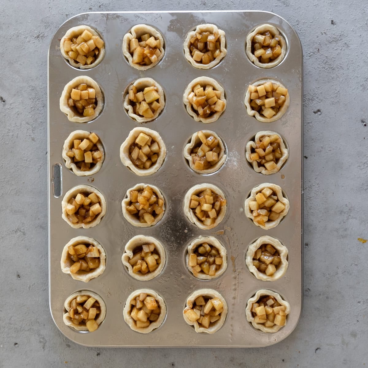 Mini apple pies in a muffin tin before being baked.