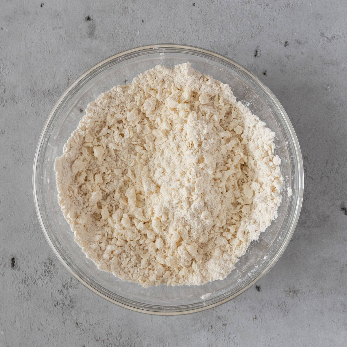 the dry ingredients and butter combined in a glass bowl on a grey background.